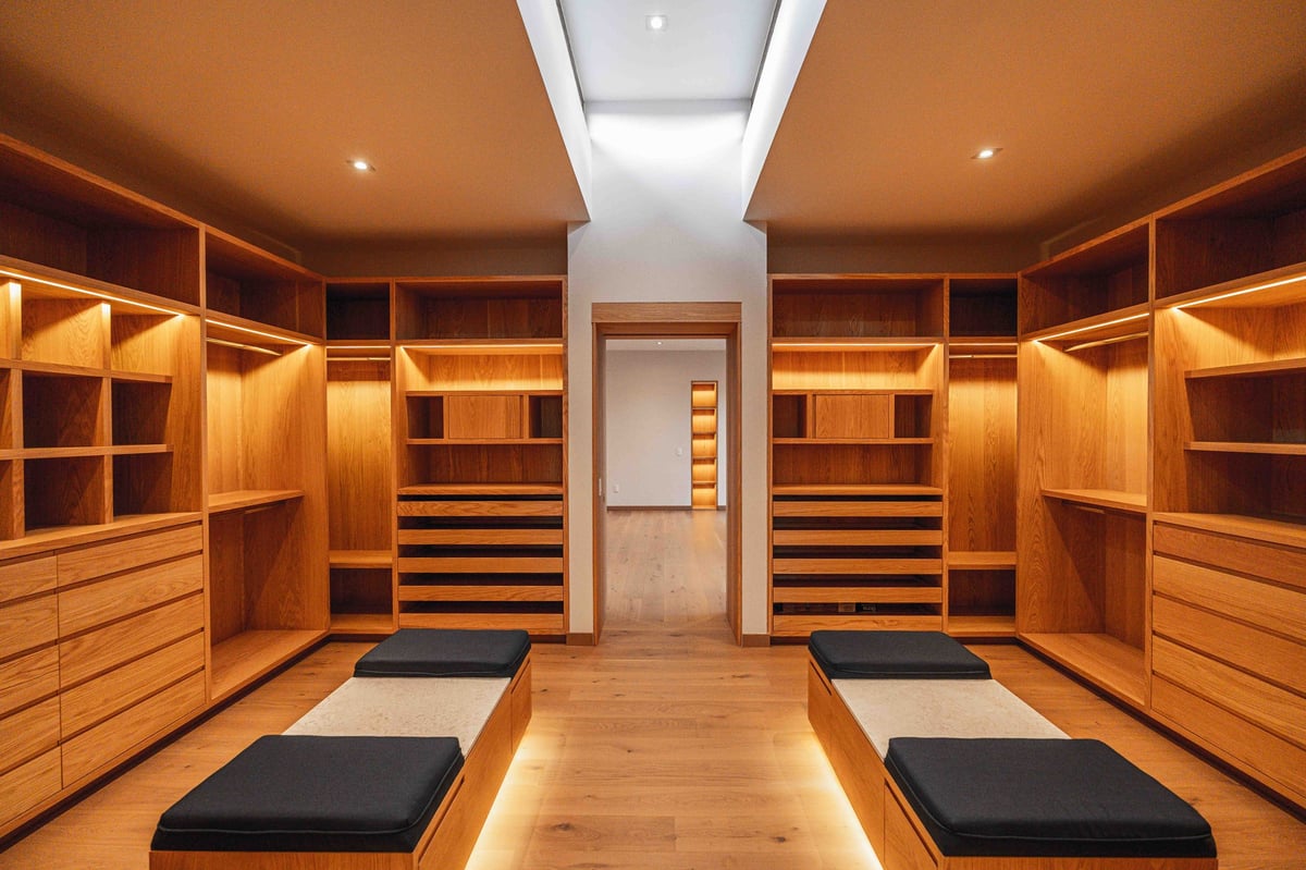 Luxurious wooden walk-in closet with built-in shelving, drawers, central seating, and warm ambient lighting