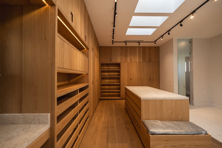 Modern walk-in closet with warm wood cabinetry, built-in drawers, shelving, and skylights overhead