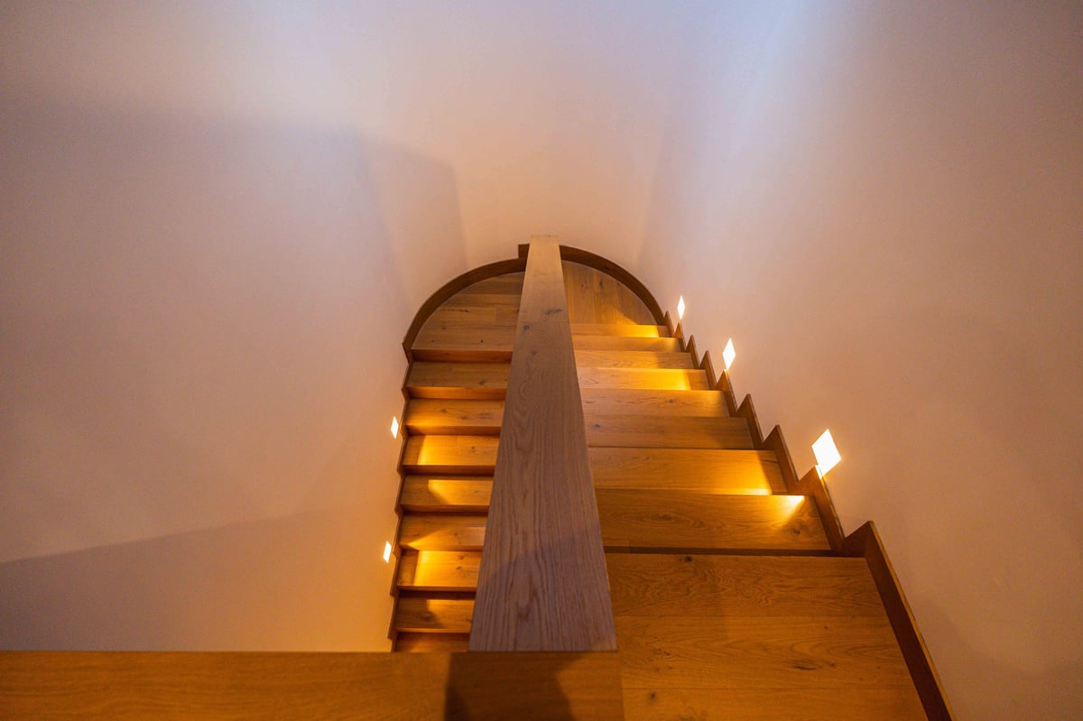 Wooden staircase with warm lighting mounted on wall, featuring decorative cone-shaped centerpiece