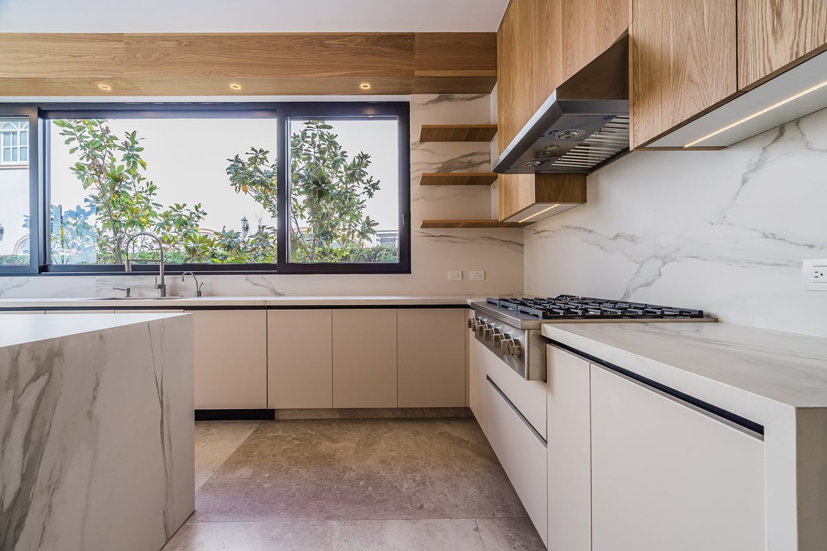 Modern kitchen with white cabinetry, marble countertops, gas range, and large windows overlooking greenery
