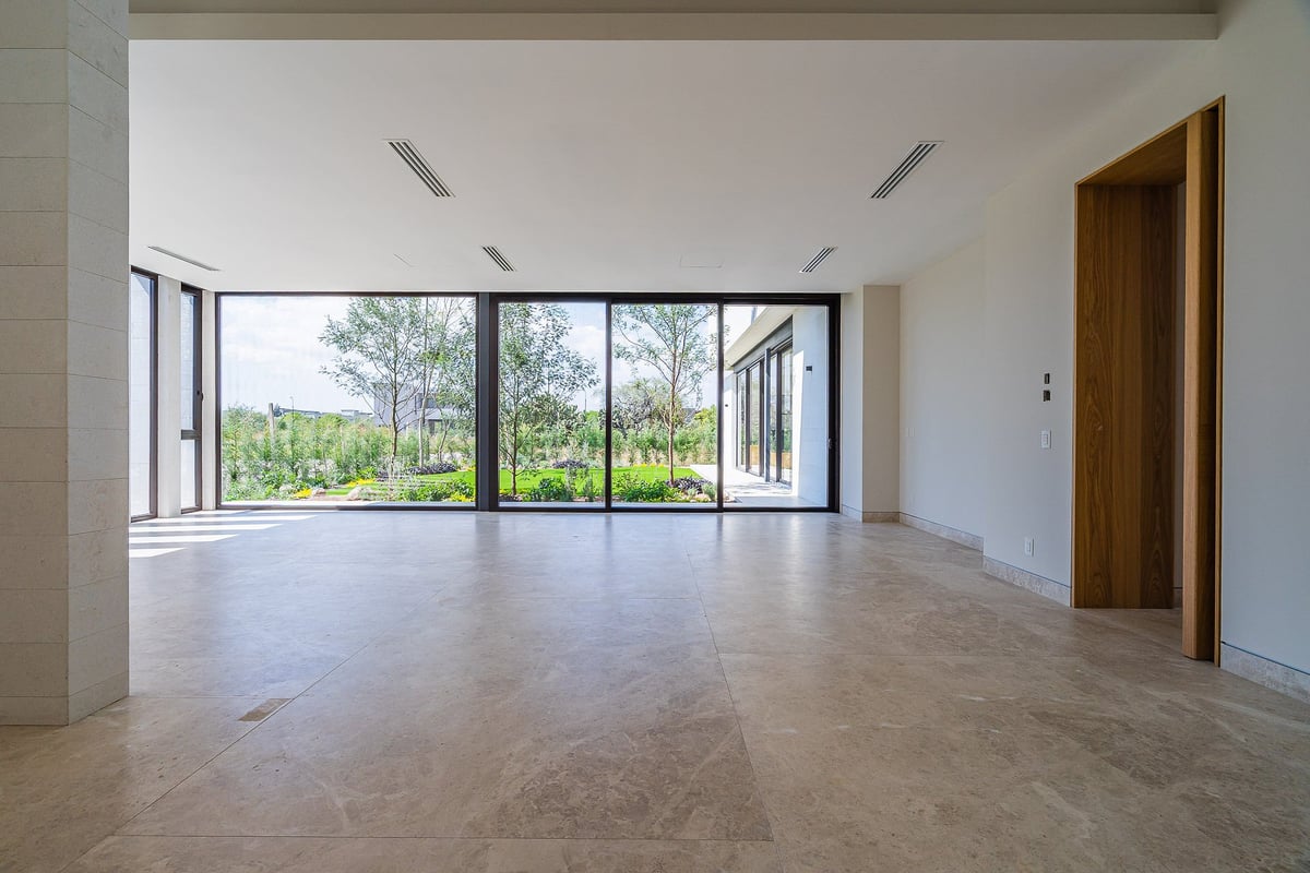 Empty modern living room with large glass doors, marble flooring, recessed lighting, and views of green trees outside