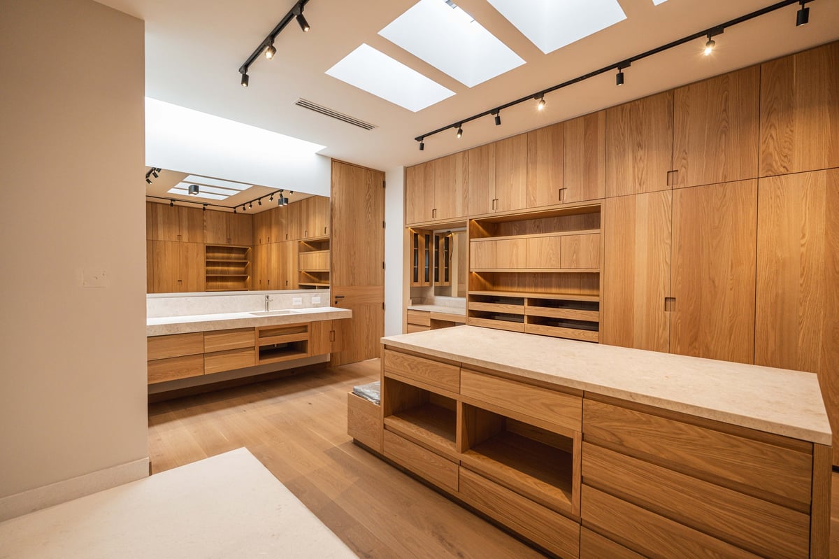 Modern walk-in closet with wooden cabinetry, white quartz countertops, skylight, and track lighting throughout