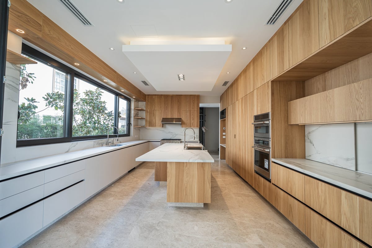 Modern kitchen with light wood cabinetry, white countertops, central island, and large windows overlooking greenery