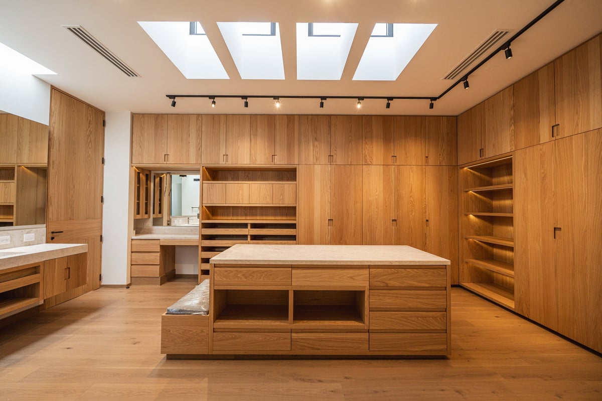 Luxury wooden walk-in closet with built-in cabinetry, central island bench, skylights, and warm ambient lighting
