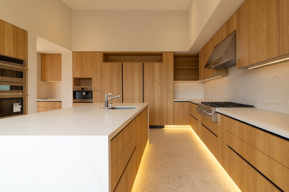 Modern kitchen with wooden cabinetry, white countertops, and warm ambient floor lighting