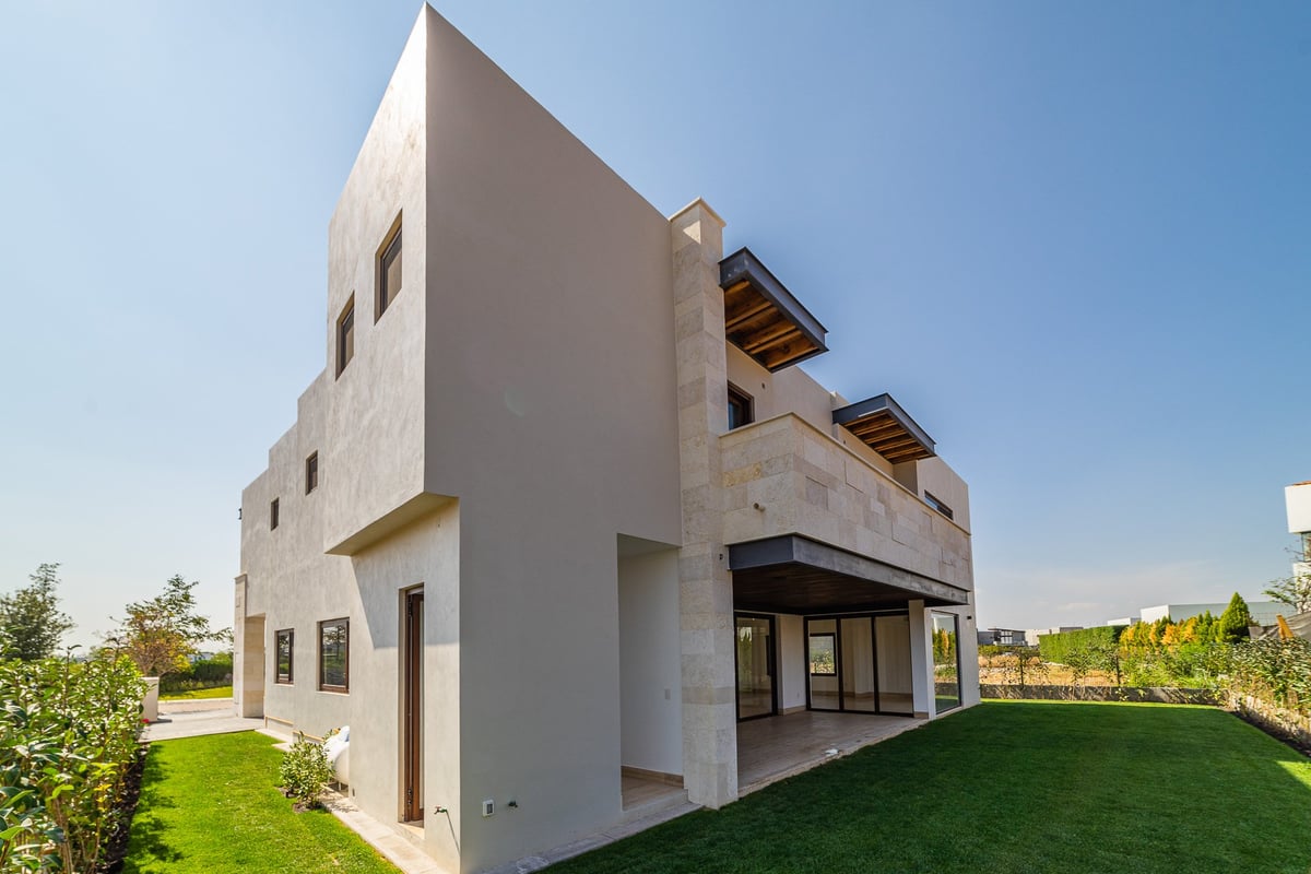 Modern white geometric house with multi-level design, large windows, and manicured lawn under clear blue sky