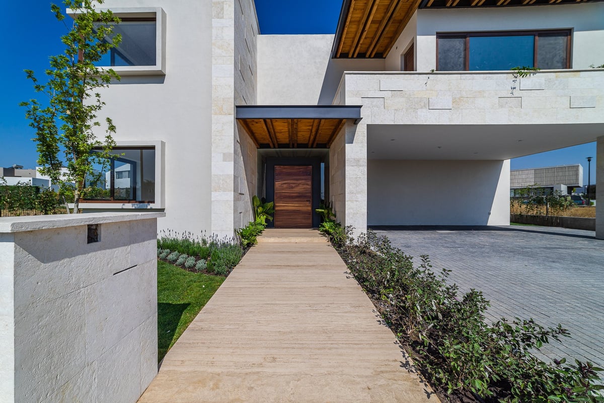 Modern white house with wooden entry walkway, dark wood door, and integrated garage under clear blue sky