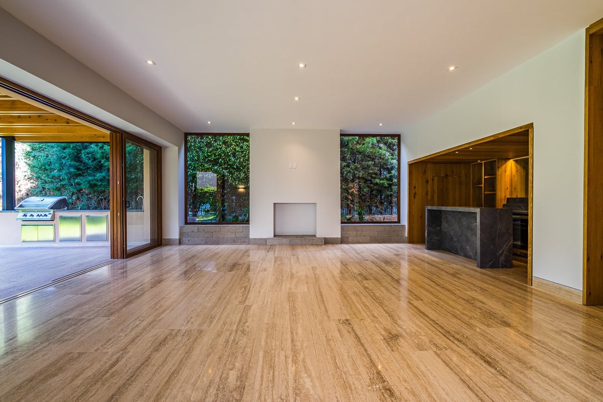 Empty modern living room with wooden floors, large windows, recessed lighting, and wood-paneled features