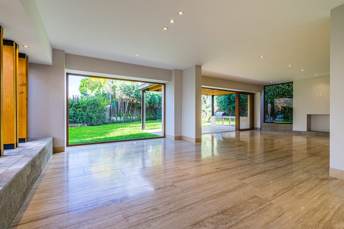 Spacious modern interior with wooden flooring, large glass doors overlooking a garden, recessed lighting, and minimalist decor