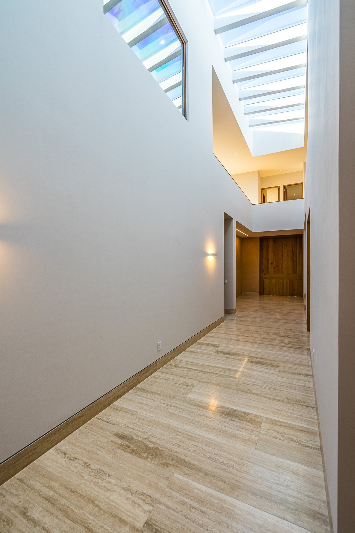 Modern hallway with wooden flooring, white walls, and skylights illuminating the bright corridor leading to a yellow-lit room