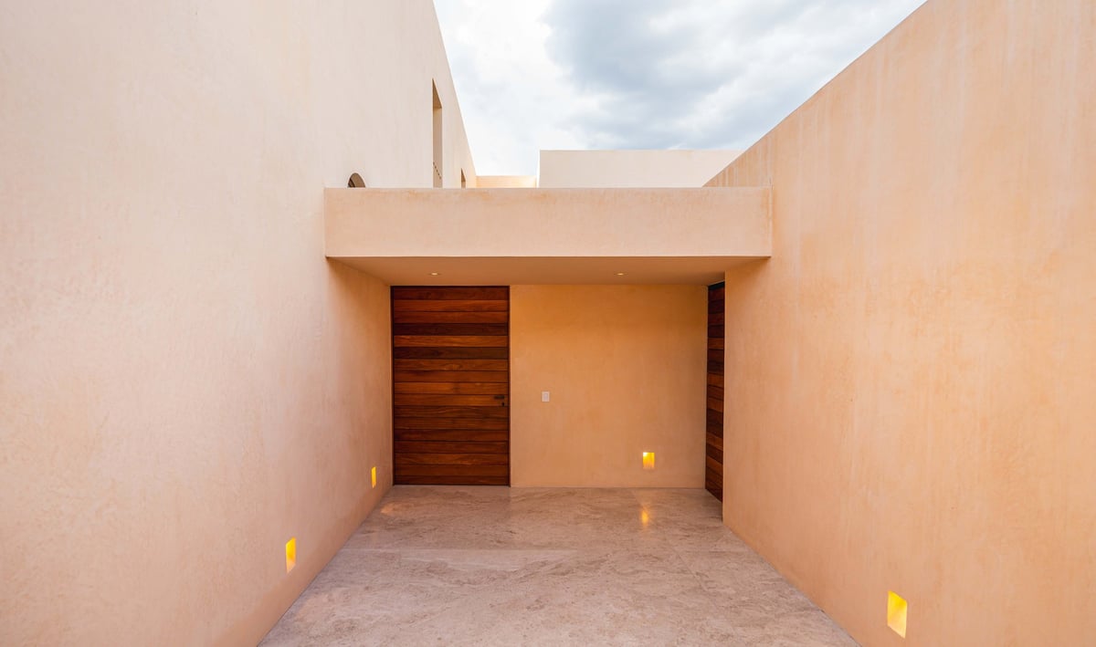 Empty beige room with concrete floor, wooden door, and skylight opening to cloudy sky