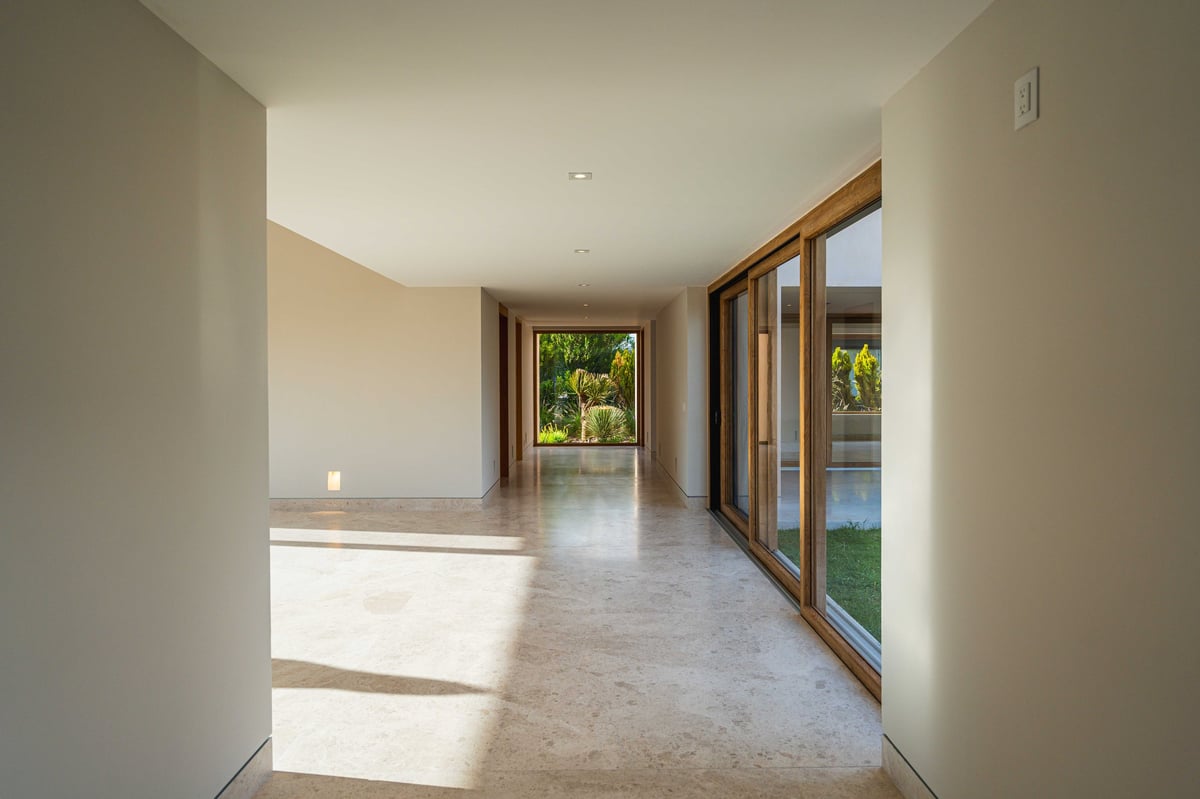 Empty modern hallway with polished floor, white walls, wooden door frame, and glass doors opening to outdoor views