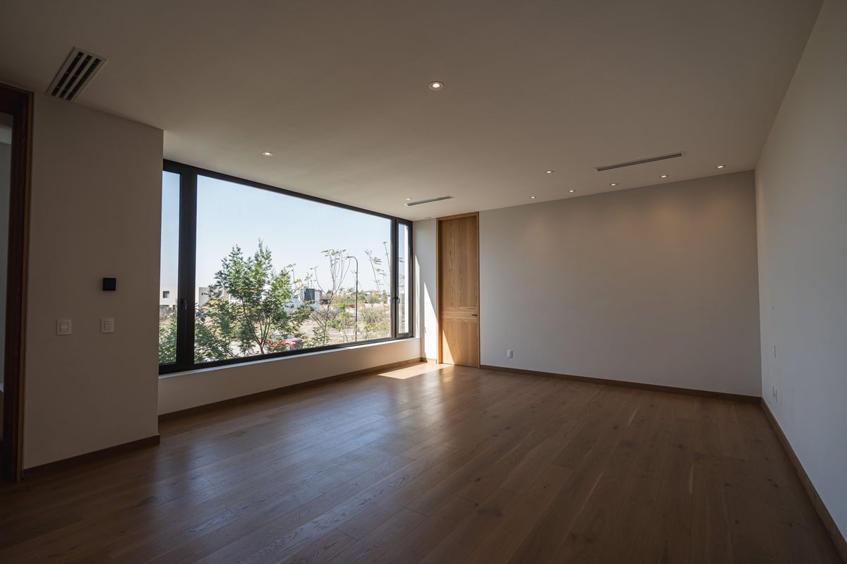 Empty modern apartment interior with dark wood floors, white walls, and large window overlooking cityscape