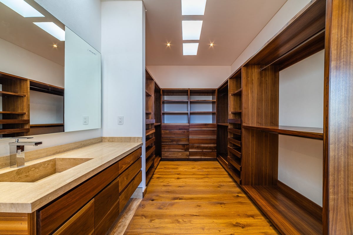 Modern luxury walk-in closet with wood cabinetry, marble countertop, shelving, and hardwood flooring