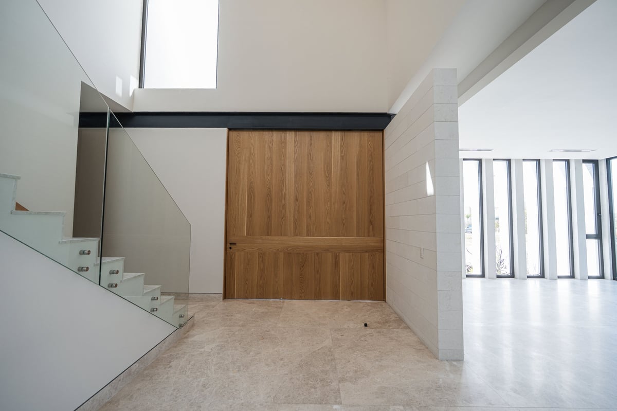 Modern minimalist interior with wooden door, white walls, gray tile floor, staircase, and skylights