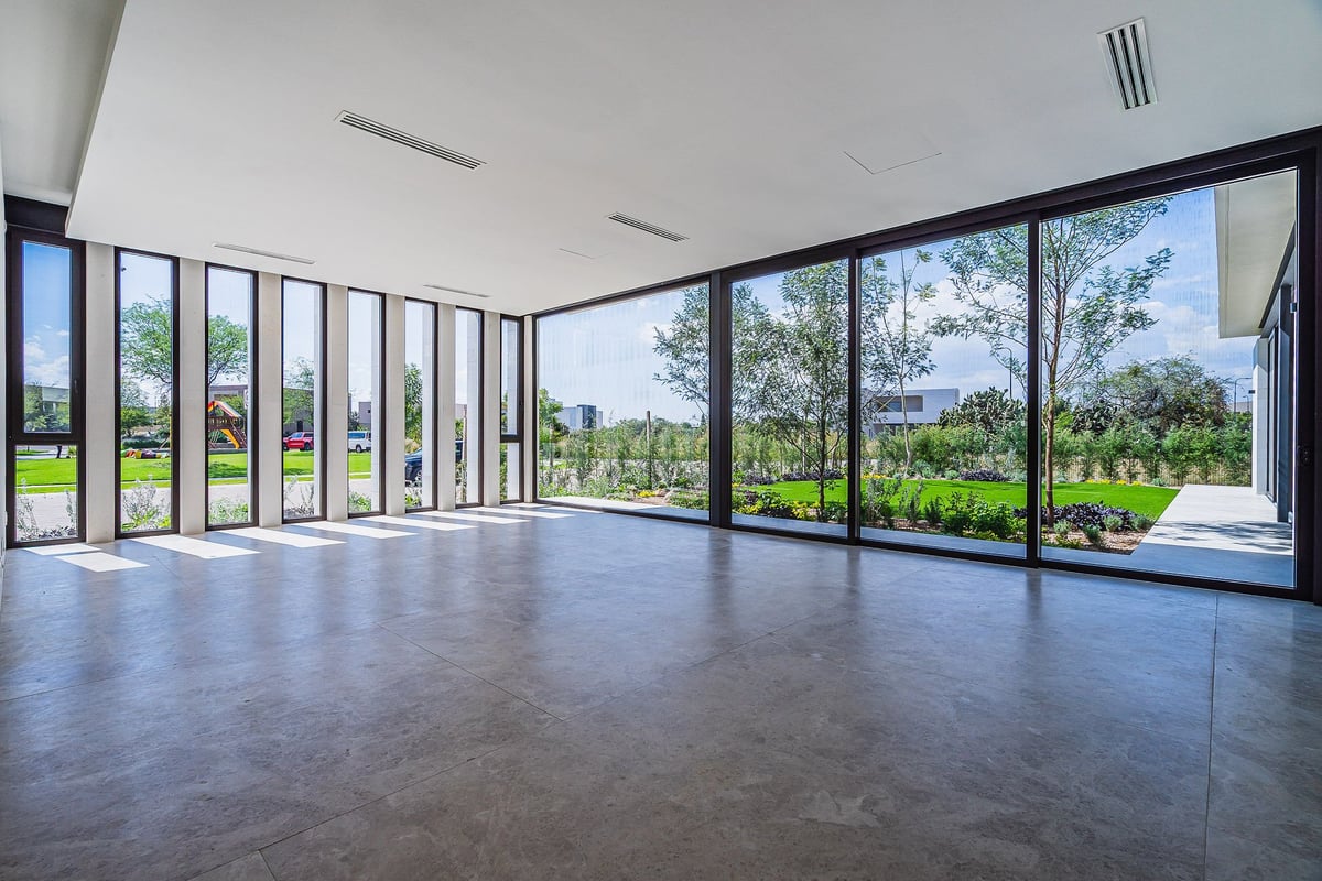 Modern empty room with polished concrete floor and floor-to-ceiling windows overlooking green landscape