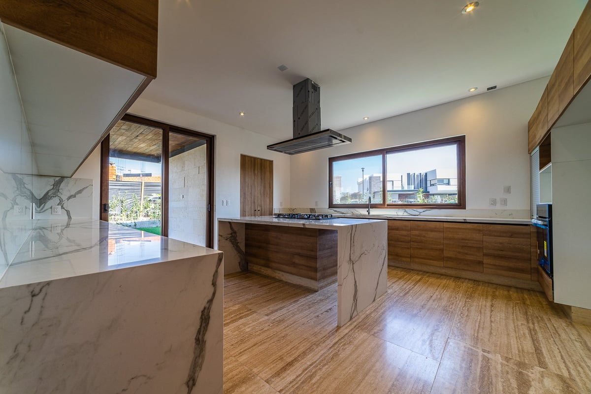 Modern kitchen with wood cabinetry, marble countertops, stainless steel range hood, hardwood flooring, and large windows overlooking the city