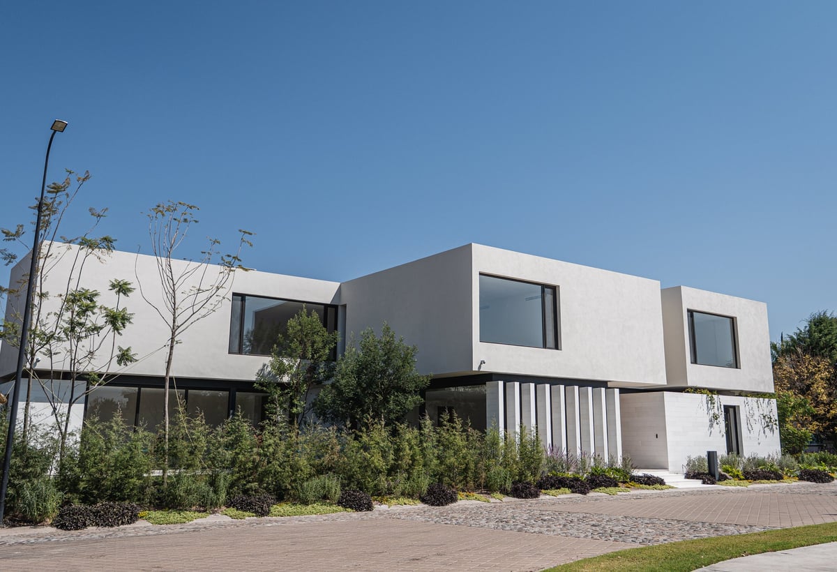 Modern two-story residential house with white and gray exterior, large windows, and landscaping