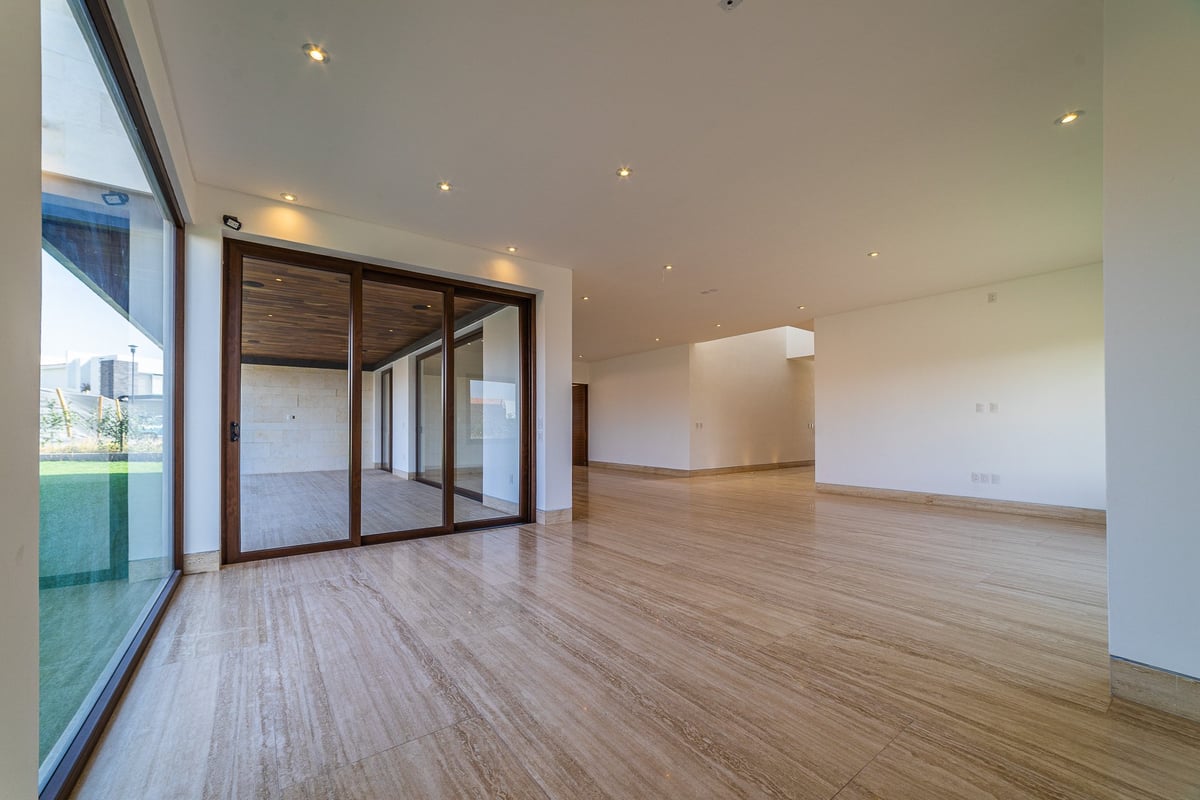 Empty modern apartment interior with wooden flooring, large windows, glass sliding doors, recessed lighting, and white walls