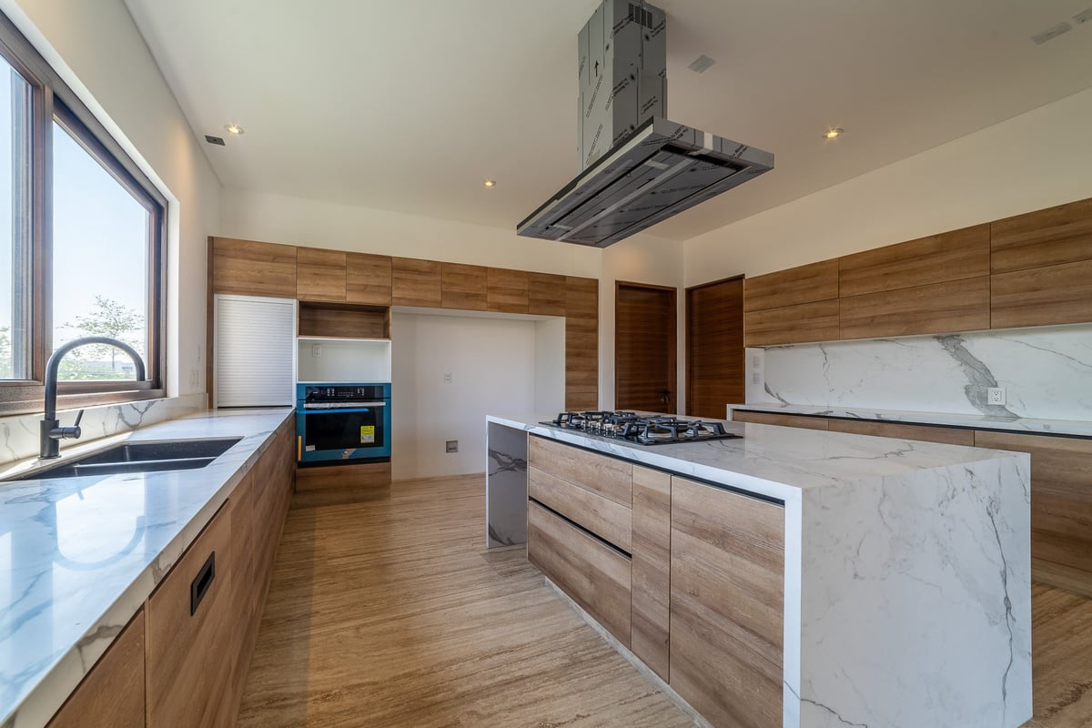 Modern kitchen with wood cabinetry, marble countertops, island, stainless steel appliances, and skylight