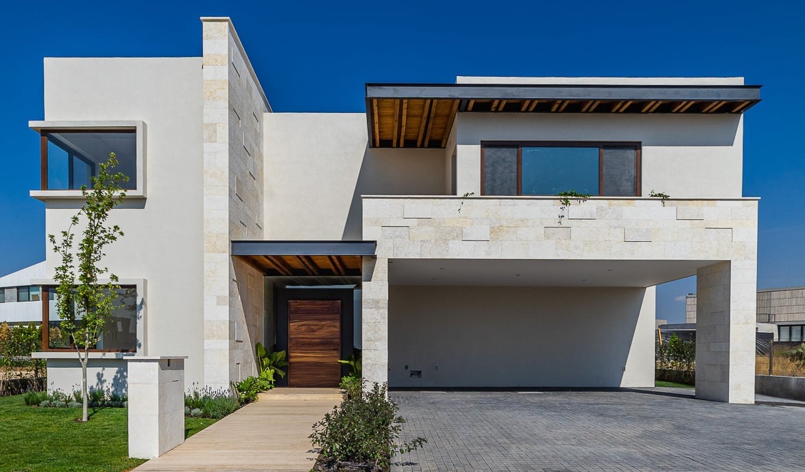 Modern white cubic house with garage, wooden accents, and landscaping against blue sky