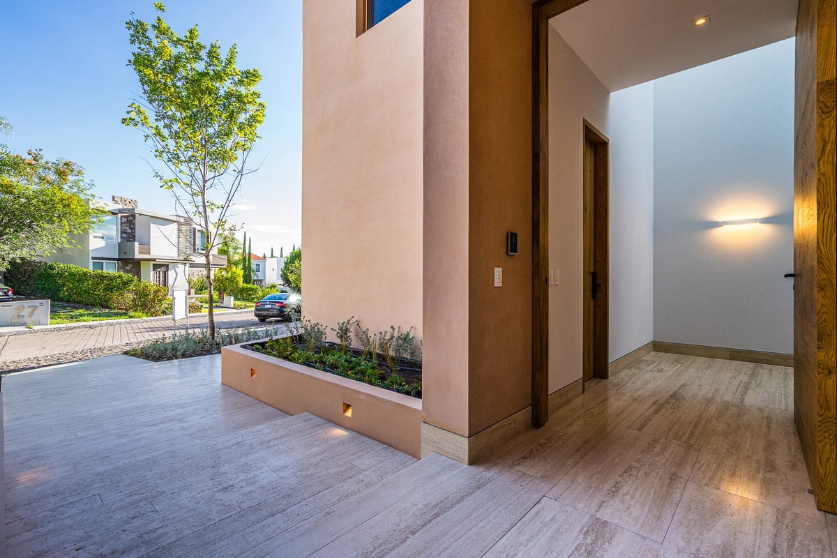 Modern entryway with wooden deck, pink-beige exterior walls, large window, and manicured landscaping visible from the porch