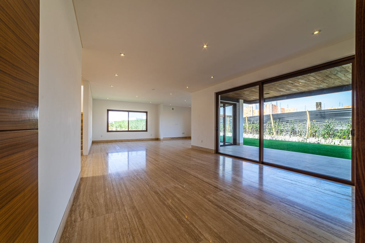 Modern empty living space with wood flooring, white walls, recessed lighting, and large glass doors opening to a green landscape view