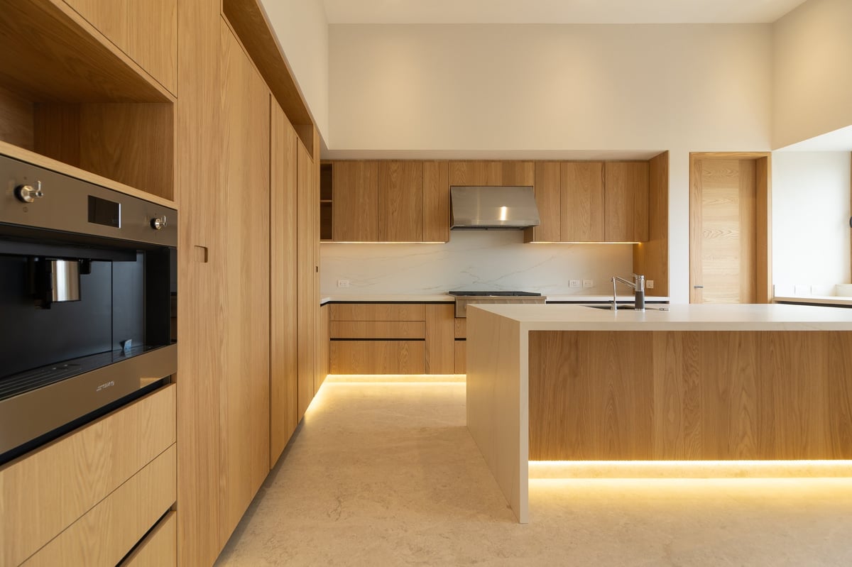 Modern wooden kitchen with light wood cabinetry, stainless steel appliances, white countertops, and ambient under-cabinet lighting