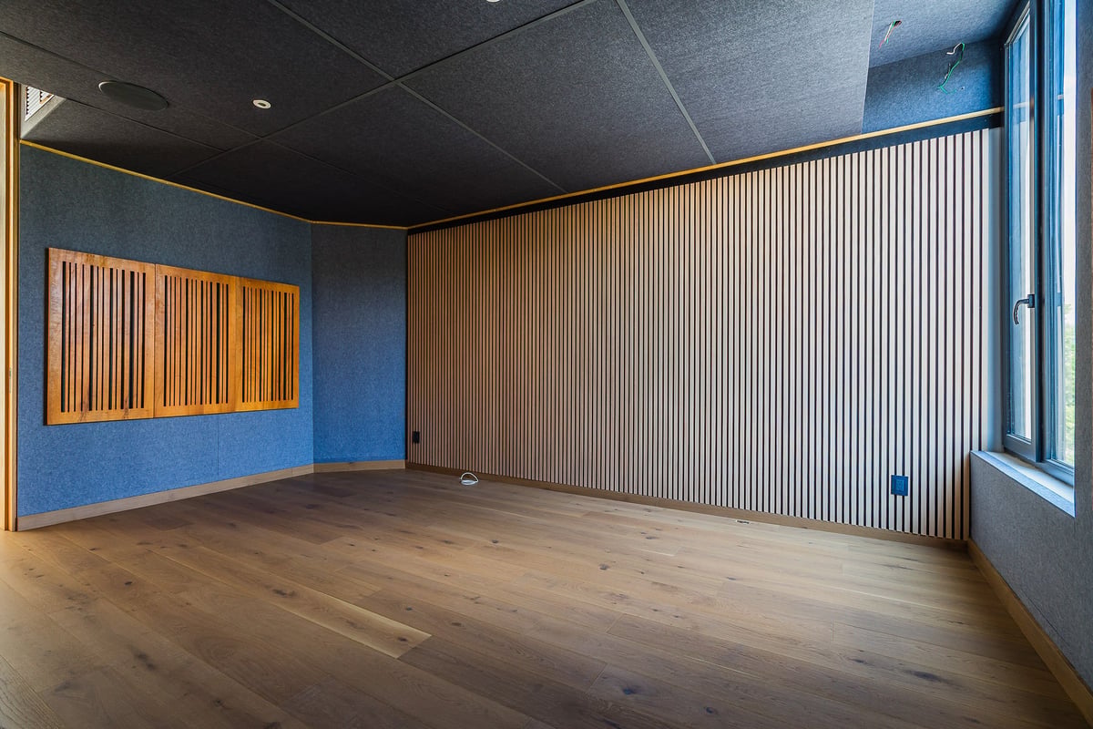Empty modern art gallery or studio space with wooden floor, blue walls, yellow-framed artwork, corrugated metal wall, and ceiling lighting