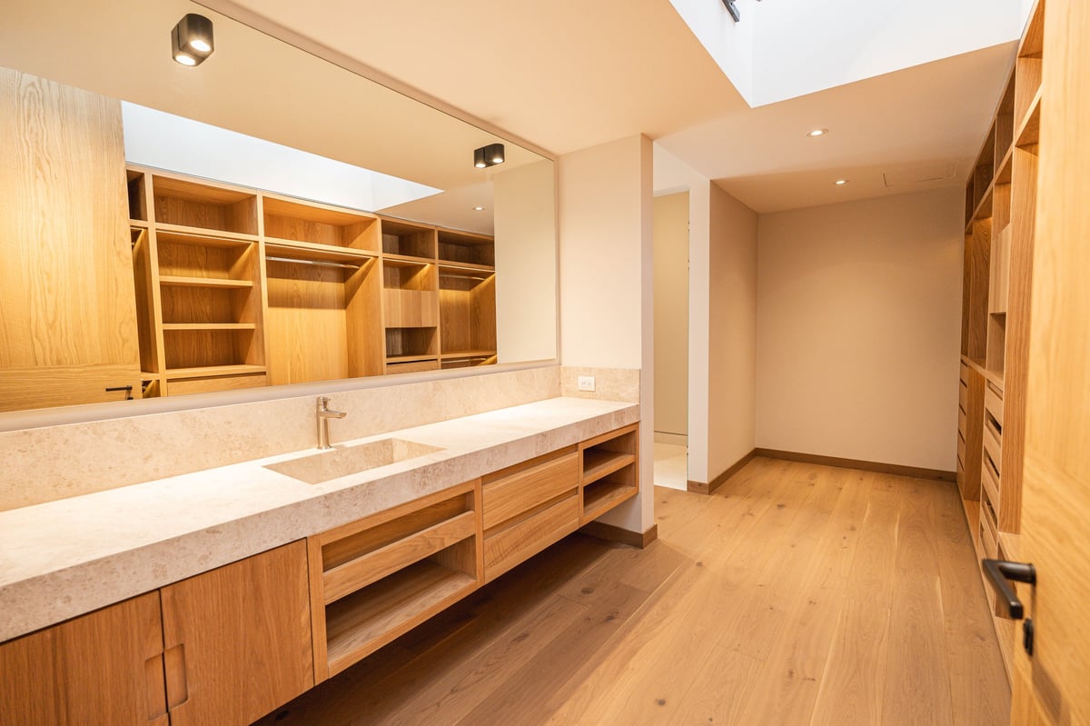 Spacious modern bathroom with wooden cabinetry, long vanity with marble countertop, large mirror, and hardwood floors